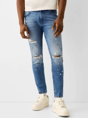 Bershka Jeansy Skinny Z Przetarciami I Plamami Farby Mężczyzna Niebieski