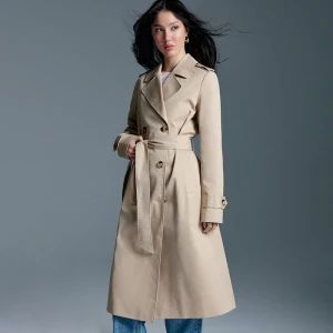 Długi beżowy trencz z paskiem i dwurzędowym zapięciem House