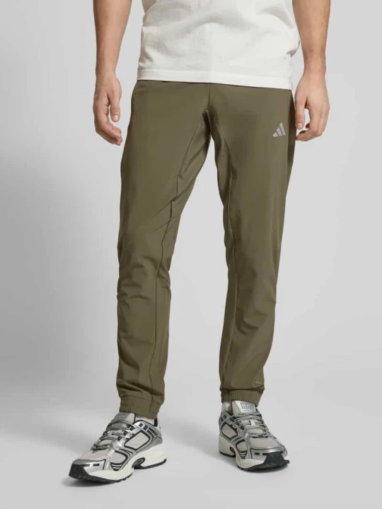 Zdjęcie produktu Spodnie dresowe o kroju regular fit z elastycznym pasem z nadrukiem z logo Model 'TECH APP S-PANT' Adidas Oliwkowy