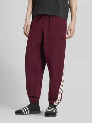 Spodnie dresowe o kroju regular fit z kieszeniami zapinanymi na zamek błyskawiczny Adidas Ciemnoczerwony